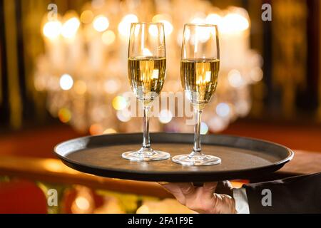 Kellner serviert Sektgläser auf einem Tablett in ein feines Restaurant, ein großer Kronleuchter im Hintergrund Stockfoto