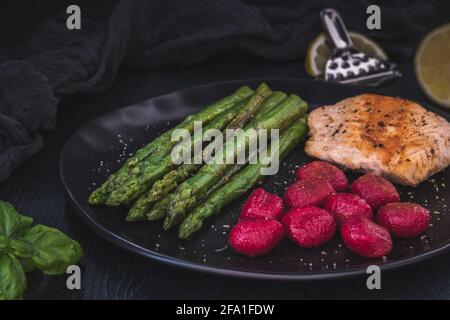 Gegrillter grüner Spargel und Lachs mit Rote Beete-Gnocchi auf Schwarz Hintergrund Stockfoto