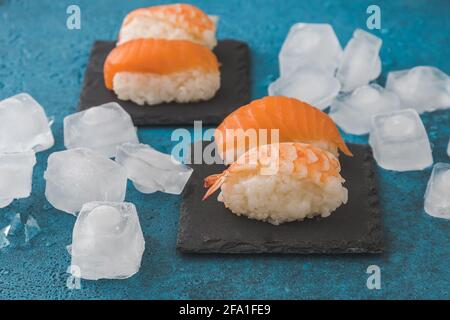 Nigiri Sushi auf Schiefer mit Eiswürfeln auf blauem Hintergrund Stockfoto