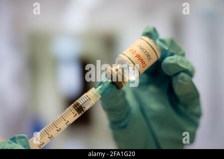 Arzt, Krankenschwester mit blauen Handschuhen wählt Coronavirus-Impfstoff von einer Ampulle in eine Spritze, mit verschwommenem Krankenhaushintergrund. Stockfoto