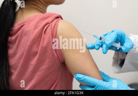 Krankenschwester, Arzt oder Allgemeinmediziner in blauen Handschuhen, die Spritze halten, um jungen weiblichen Patienten in einem roten Hemd in der Klinik Injektionen oder Impfungen zu machen. Stockfoto