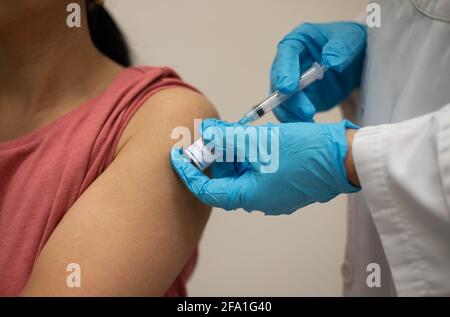 Krankenschwester, Arzt oder Allgemeinmediziner in blauen Handschuhen, die Spritze halten, um jungen weiblichen Patienten in einem roten Hemd in der Klinik Injektionen oder Impfungen zu machen. Stockfoto