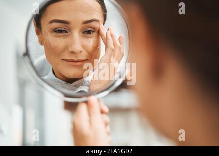 Spa-Kundin mit einem Handglas, das ihr Gesicht berührt Stockfoto