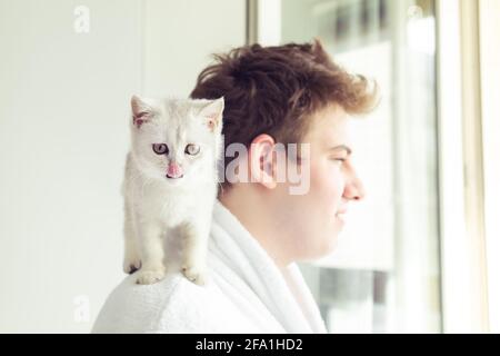 Weißes Kätzchen, das auf der Schulter des Mannes sitzt. Am frühen Morgen, Sonnenschein. Selektiver Fokus auf die Katze. Stockfoto