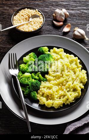 Brokkoli Kartoffelpüree mit gehackten Mandeln bestreut serviert mit gedünsteten Brokkoli blüsst auf einem schwarzen Teller auf einem dunklen Holz Tabelle Stockfoto