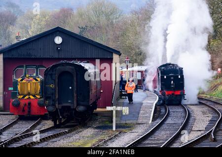 Historische Dampfeisenbahn oder Lok, die Rauchwolken aufblähen (Leute auf dem Bahnsteig, Eisenbahner, Maschinenschuppen) - Oxenhope Station Sidings, Yorkshire, England Großbritannien. Stockfoto