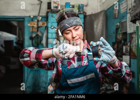 Porträt einer jungen Mechanikerin in Uniform, die ein Teil mit einem Schraubendreher fixiert. Garage im Haus. Stockfoto