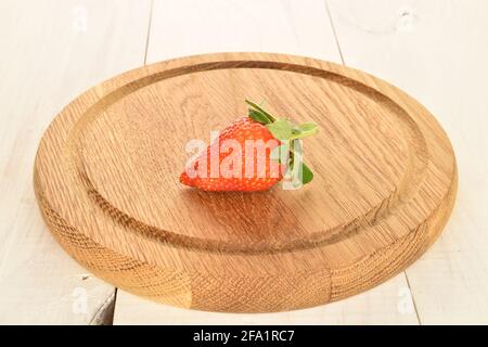 Eine Bio-Erdbeere auf einem Bambustablett, auf einem bemalten Holztisch. Stockfoto