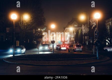 Avenue (Straße) während einer regnerischen Nacht in München, Bayern, Deutschland. Verkehrszeichen und Kreisverkehr. Scheinwerfer und Stau beleuchten die Stadt. Stockfoto