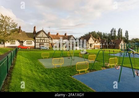 Dorfgrün in Thornton Hough, Wirral, UK; Kinderspielplatz im Vordergrund. Stockfoto