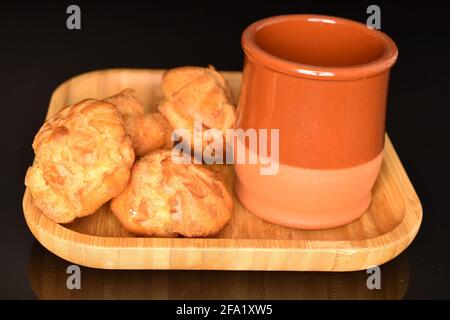 Mehrere süße Chouquettes auf einer Bambusplatte mit Tonglas, Nahaufnahme, auf schwarzem Hintergrund. Stockfoto