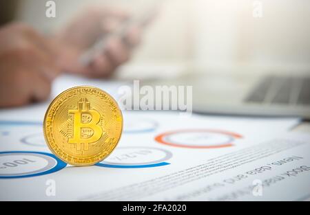 Nahaufnahme eines goldenen Bitcoins auf dem Schreibtisch mit Hintergrund eines Geschäftsmannes. Stockfoto