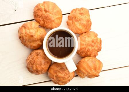 Mehrere frisch duftende Chouquettes mit einer Tasse Kaffee, Nahaufnahme, auf einem weißen Holztisch, Draufsicht. Stockfoto