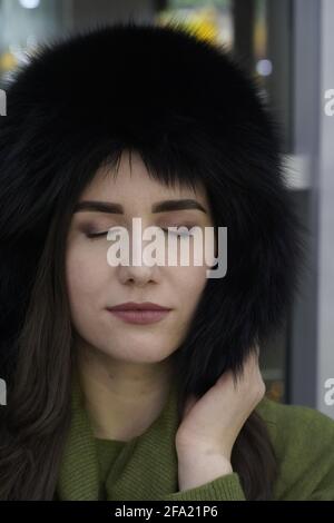 Porträt einer Frau im lässigen Stil mit geschlossenen Augen im Winterpelz Hut Nahaufnahme, Gesicht und Hände auf glitzerndem Hintergrund Stockfoto