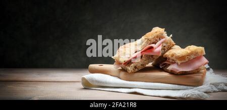 Focaccia mit Mortadella auf altem Holztisch mit Schneidebrett und Serviette, Platz für Text. Stockfoto