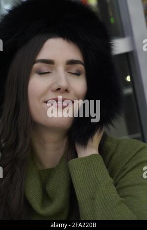 Porträt einer Frau im lässigen Stil mit geschlossenen Augen im Winterpelz Hut Nahaufnahme, Gesicht und Hände auf glitzerndem Hintergrund Stockfoto