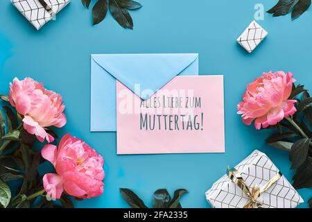 Text alles Liebe zum Muttertag bedeutet viel Liebe zum Muttertag. Grußkarten-Design mit rosa Pfingstrosen, Blättern und eingewickelten Geschenkschachteln. Flach liegend Stockfoto