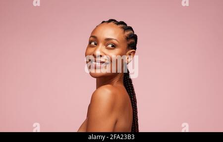 Attraktive Frau mit sauberer und klarer Haut schaut weg. Weibliches Modell mit geflochtener Frisur, die vor rosa Hintergrund steht. Stockfoto