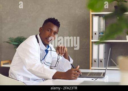 Afroamerikanischer Arzt Arzt, der mit einem Laptop am Tisch sitzt Stockfoto