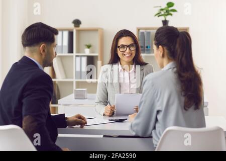 Freundlicher Versicherungsmanager oder Kreditmakler, der sich mit einem jungen Paar trifft In ihrem Büro Stockfoto