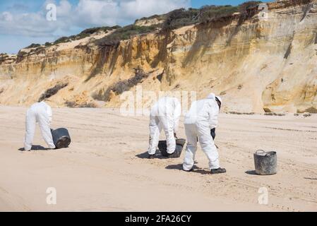 Konzept: Reinigung der Küste. Eine Gruppe von Personen, die nicht erkennbar sind. Arbeiter mit persönlicher Schutzausrüstung (PSA), die nach einer Kraftstoff-spi den Strand reinigen Stockfoto