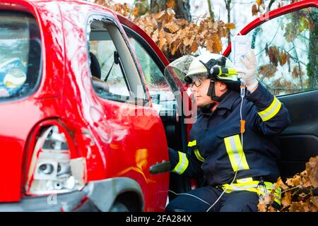 Unfall - Feuerwehr rettet Unfall Opfer eines Autos, Feuerwehrmann hält einen Tropf für Infusion Stockfoto