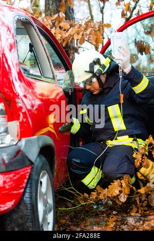 Unfall - Feuerwehr rettet Unfall Opfer eines Autos, Feuerwehrmann hält einen Tropf für Infusion Stockfoto