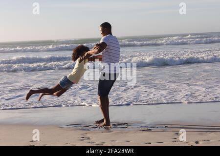 afroamerikanischer Vater und Tochter, die Spaß beim Spinnen haben Strand Stockfoto