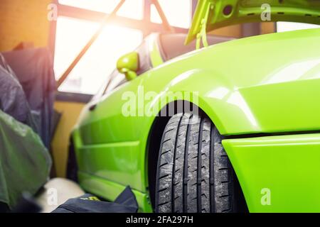 Nahaufnahme Detailansicht Rad von benutzerdefinierten getunten Street Sportwagen Rennwagen in der Tankstelle Garage mit geöffneter Haube gegen hinterleuchtete Sonnenfenster. Auto Stockfoto