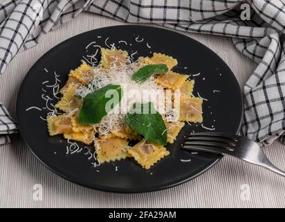 Ein köstliches Gericht aus kleinen Ravioli, gefüllt mit Fleisch, gekrönt mit Butter, Salbeiblättern und geriebenem Parmesan, einem typisch italienischen Gericht Stockfoto