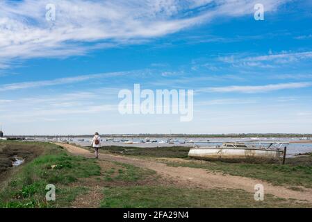 Mersea Island Essex, Rückansicht einer Frau, die auf dem Küstenpfad entlang der Schwarzwassermündung des Flusses, Mersea Island, Essex, Großbritannien, läuft Stockfoto