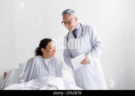 Lächelnder Arzt zeigt digitale Tablette erfreut afroamerikanische Frau In der Klinik Stockfoto