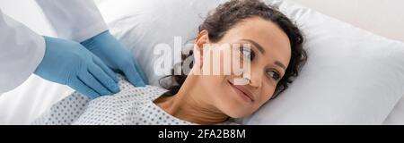 Arzt in Latexhandschuhen untersucht Schulter einer lächelnden afroamerikanischen Frau, Banner Stockfoto