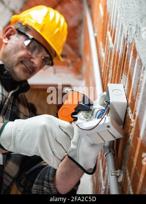 Elektriker mit Abisolierer bereitet elektrische Kabel vor; tragen Sie Helm, Handschuhe und Schutzbrille. Sicherheit am Arbeitsplatz. Stockfoto