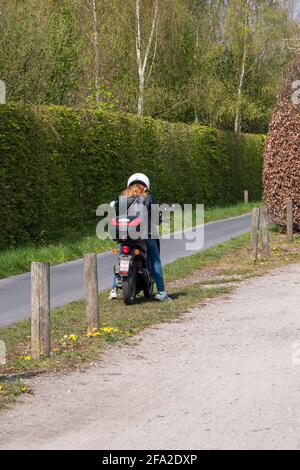 Sint Gillis Waas, Belgien, 21. April 2021, Mädchen auf dem Roller hält an und schaut auf ihr Smartphone Stockfoto