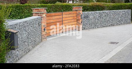 Haus vor Garten Grenzmauer aus Gabion Drahtkäfig gebaut Gefüllt mit im Käfig gebrochenem Stein mit Ziegel Piers & Holz Eingangstore England GB Stockfoto