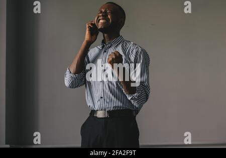 Schwarzer Kerl auf grauem Hintergrund, der am Telefon spricht Happy erfährt die gute Nachricht Stockfoto