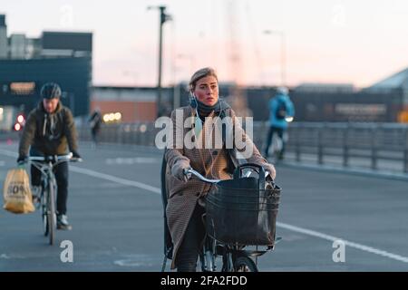 Kopenhagen, Dänemark 29. November 2019. Frau im karierten Mantel fährt mit dem Fahrrad und hört Musik von kabelgebundenen Kopfhörern. Menschen in Kopenhagen, lifestyl Stockfoto