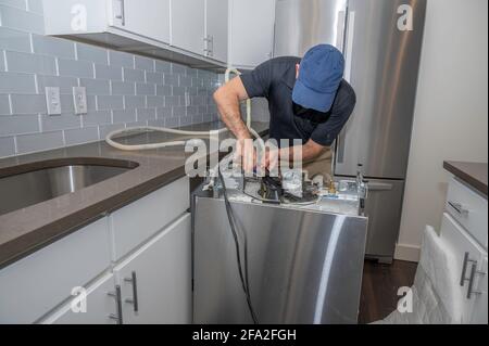 Der Mechaniker arbeitet an einem Geschirrspüler, der die Wasserschläuche installiert Stockfoto