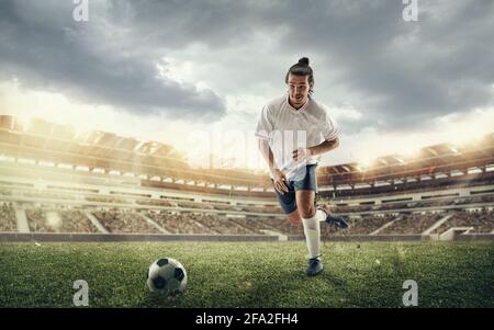 Männlicher Fußball, Fußballspieler, der während eines Sportspiels im Stadion im Sprung den Ball auf dem Hintergrund des dunklen Himmels erhaelt Stockfoto