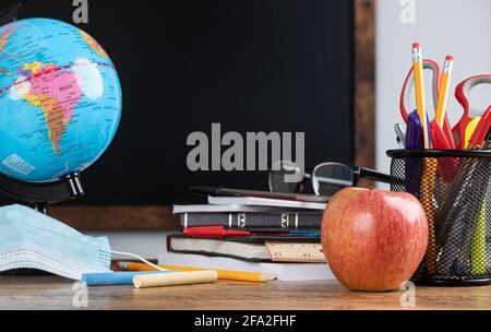 Schreibtisch im Klassenzimmer mit Schulbedarf und leerer Tafel im Hintergrund Stockfoto