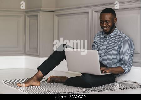 Schwarzer junger Mann, der mit einem Laptop auf dem Boden sitzt Und arbeiten Stockfoto