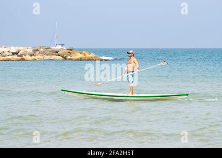 Tel Aviv, Israel - 17. April 2021: Ein junger Mann auf einem Surfbrett in der Nähe des Strandes von Tel Aviv, Israel, an einem klaren, sonnigen Tag. Stockfoto