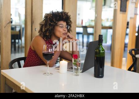 Frau mit gemischter Rasse, die im Restaurant am Tisch sitzt und Video hat Anruf senden Schlag Kuss Stockfoto