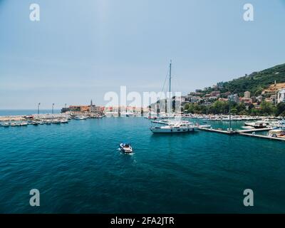 Das weiße Motorboot fährt am Pier der Stadt vorbei Von Budva Montenegro auf dem Hintergrund von alten Gebäuden Stockfoto