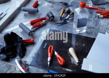 Arbeitswerkzeuge in roten und schwarzen Farben auf dunklem Tisch. Linolschnitt-Konzept. Schneidwerkzeuge, Tintenroller und andere Werkzeuge für die Linolschnitt-Herstellung. Hochwertige Fotos Stockfoto