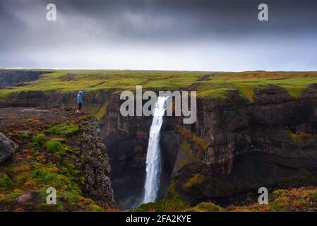 Wanderer, der am Rande des Haifoss Wasserfalls steht Island Stockfoto