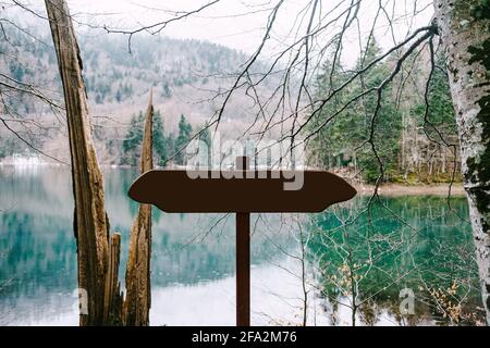 Unmarkiertes Straßenschild steht in der Nähe eines Sees im Wald Vor einem Hintergrund von Bergen Stockfoto