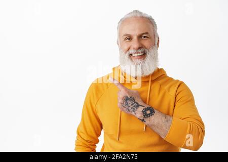 Lächelnder alter Mann mit Tattoos in der linken oberen Ecke. Cooler Granfather mit langem Bart und orangefarbenem Hoodie, der Werbung für Werbezwecke zeigt Stockfoto