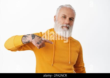 Cooler älterer Mann mit Tattoos, die auf sich zeigen. Bärtiger, cooler Großvater in orangefarbenem Kapuzenpullover, der sich selbst für seine Leistung ausgibt und sich mit ihm brüskiert Stockfoto